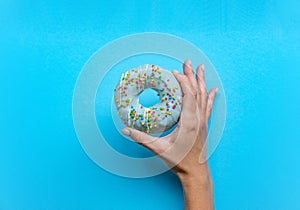 One donut with blue icing. An overhead view of a doughnut with colored sprinkles. Female hand holding donut over blue