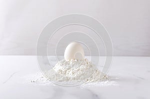One egg on the heap of flour on the kithen whit table.Ingredients for baking products