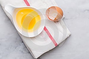 One egg yolk in white bowl and broken egg shells