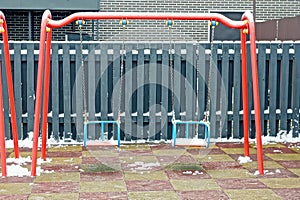 One empty red metal swings on a playground in white snow