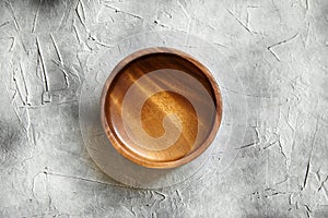 One empty wooden bowl on grey background. Single round salad bowl on stone table, top view