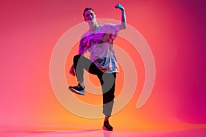 One energetic young man hip-hop dancer training isolated over gradient pink background in neon light