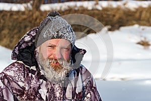 One euriopean bearded fisher man or hunter with ice and hoarfrost on beard is looking to the camera with smile