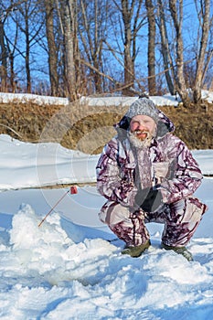 One euriopean bearded man is fishing close to hole at winter sunny day under blue sky