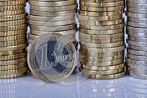 A one euro coin in front of many more coins stacked in columns o