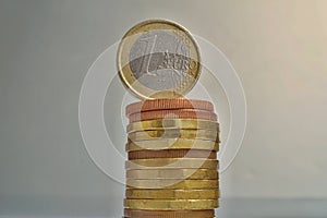 One Euro European currency EUR coin on the top of of tall pile of metal coins in golden and copper color