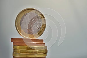 One Euro European currency EUR coin on the top of of tall pile of metal coins in golden and copper color