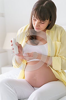 One european pregnant woman with smile is using moisturizing cream on her tummy for prevent stretch marks from pregnancy while she