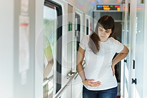 One european pregnant woman in t-shirt is getting back and belly pain while traveling by railway