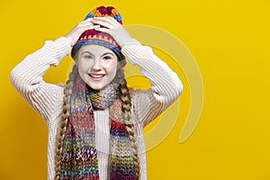 One Exclaiming Caucasian Teenage Blond Girl In Warm Hat and Scarf Posing with Lifted Hands And Laughing Against Yellow Background