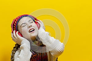 One Expressive Winsome and Smiling Caucasian Blond Girl In Warm Knitted Hat and Scarf While Listening to Music in Wireless