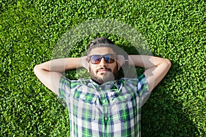 One fashion middle eastern man with beard, fashion hair style is resting on beautiful green grass day time.