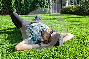 One fashion middle eastern man with beard, fashion hair style is resting on beautiful green grass day time.