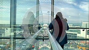 One female tourist with a backpack stands in the airport lounge, looks out the window, travel concept