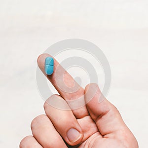 One Finger Holding A Blue Pill On White Wooden Background