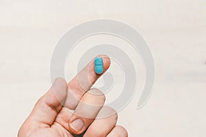 One Finger Holding A Blue Pill On White Wooden Background