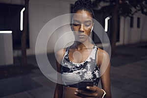 One fit young mixed race woman listening to music with wireless earphones from a cellphone while taking a break from