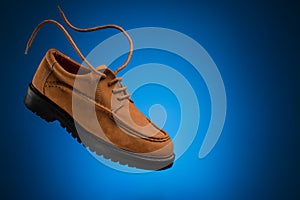 One flying leather boat shoes of wheat or brown nubuck with flying laces on a blue background