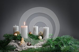 One of four candles is burning for the first Advent on fir branches with Christmas decoration against a grey background, copy