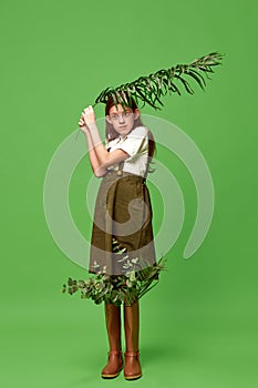 One funny little girl standing with plant leaf instead umbrella over green background. During the rain