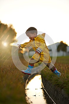 One giant leap for boykind. a little boy jumping over some water while playing outside.