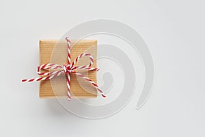 One gift box wrapped in craft paper with striped baker`s twine bow on white background. Top view, flat lay, copy space