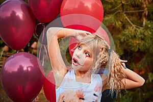 One girl aged 9 in a Halloween dress with red and black balloons in the open air in the Park, emotions of fear, horror, surprise.