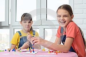 One girl laughs cheerfully, the other makes faces, children play a board game