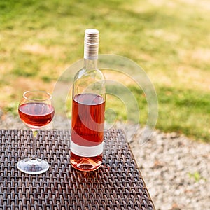 One glass and bottle of red or rose wine in autumn vineyard on wooden wicker table. Harvest time, picnic, fest theme.