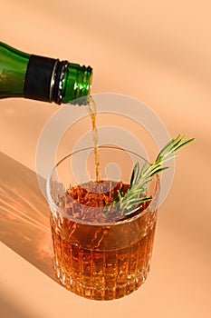 One Glass of cold whiskey garnish rosemary on beige background with sunny shadow