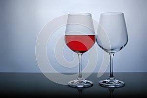 One glass half full of red wine, and the second empty on a white background