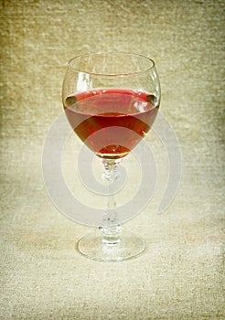 One glass with red wine against brown drapery