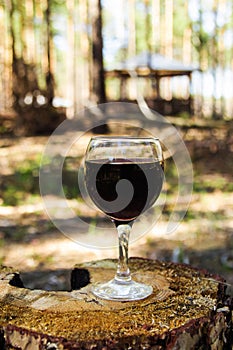One glass with a red wine on a stump on a background of a summer forest.