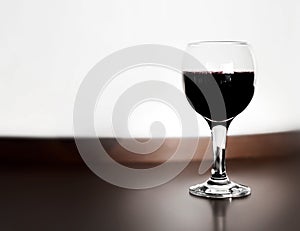 One glass of red wine wooden table and blurred white wall background. Alcohol drink on desk in room.