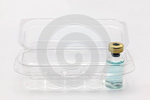 One glass vaccine bottle inside an opened translucent plastic box for ten vaccine bottles