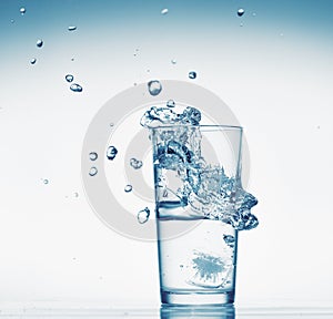 One glass of water with splash from falling ice cube, white background, isolated object
