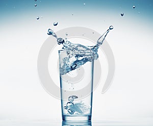 One glass of water with splash from falling ice cube, white background, isolated object
