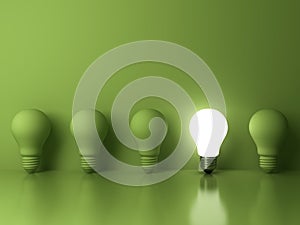 One glowing light bulb standing out from the unlit incandescent bulbs on green background with reflection