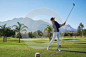 This one is going far. a focused young man hitting a golfball on a golf course outside during the day.