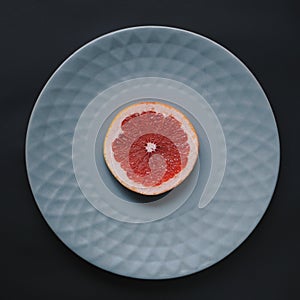 One grapefruit on gray plate on dark background.