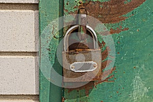 One gray metal padlock hangs on an iron green door in brown rust