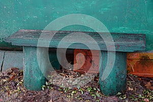 A green dirty wooden bench stands against a wall outside