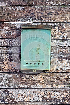 one green metal mailbox hanging from an old worn gray brown wooden fence