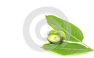 One green walnut cut and recumbent on two whole walnuts and two leaves