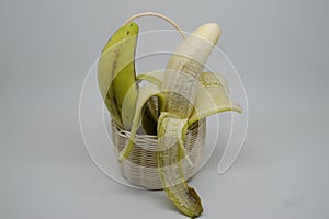 One half-peeled and one unpeeled ripe green banana (pisang ambon) served on rattan basket