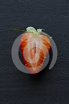 One half of strawberry, cut red beautiful strawberry close-up, on a black dark concrete background. Macro shooting. Fruit erotica photo