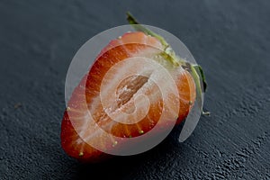 One half of strawberry, cut red beautiful strawberry close-up, on a black dark concrete background. Macro shooting. Fruit erotica photo