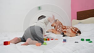 One and a half years old baby boy playing with lego blocks and soft toy dear on the bed