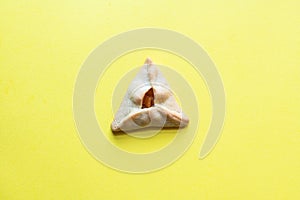 One hamantaschen cookie on yellow background. Top view