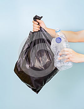 one hand holding a plastic bag filled with plastic bottles, the other holding a plastic bottle waste.isolated on blue background
